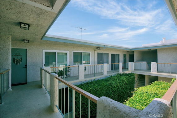 Exterior view of an apartment complex with balcony corridors and central courtyard.