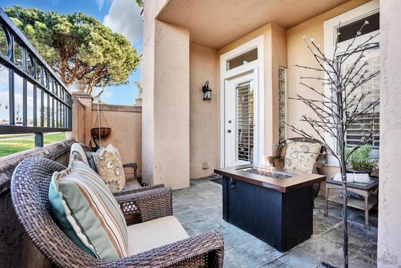 Outdoor seating area with wicker chairs and fire pit, adjacent to a building entrance with white shutters.