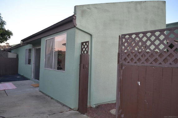 Side view of a single-story house with large windows and a fenced patio area.