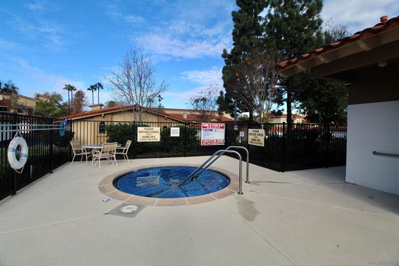 Outdoor area with a spa pool surrounded by a fence and seating.