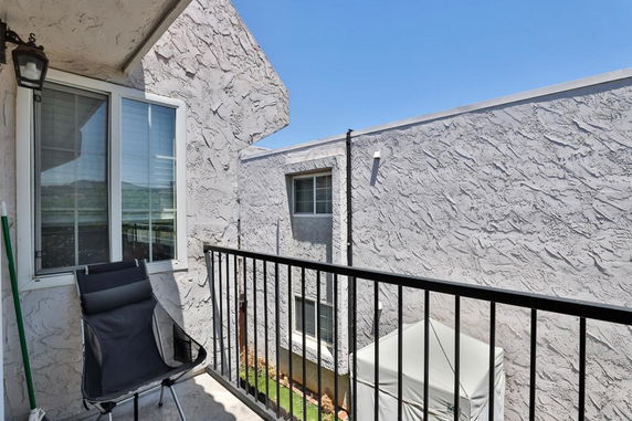 View from a balcony with a chair and railing overlooking adjacent building walls.