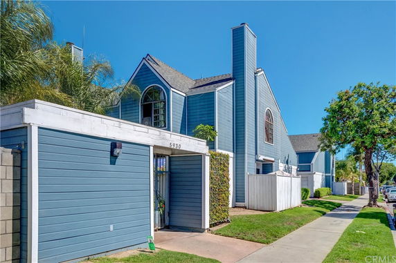 Front view of a blue two-story house with a gated entrance and a chimney.