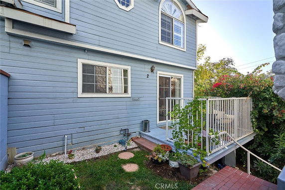 Side view of a two-story house with blue siding and a small elevated patio.