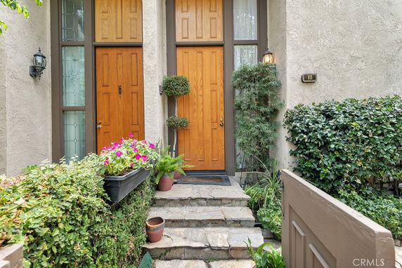 Front view of a house entrance with wooden doors and plants.