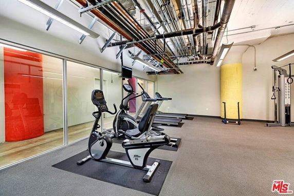 Indoor gym area with exercise equipment and exposed ceiling pipes.