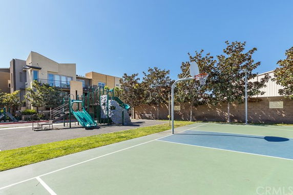 Outdoor basketball court with a children's play area featuring slides nearby.