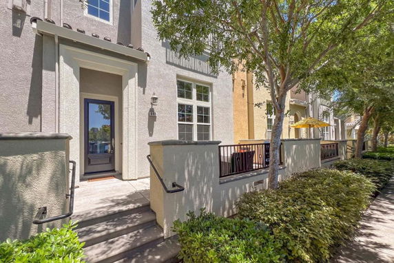 Front view of a townhouse with a small porch and steps, featuring a modern facade and a garden area.