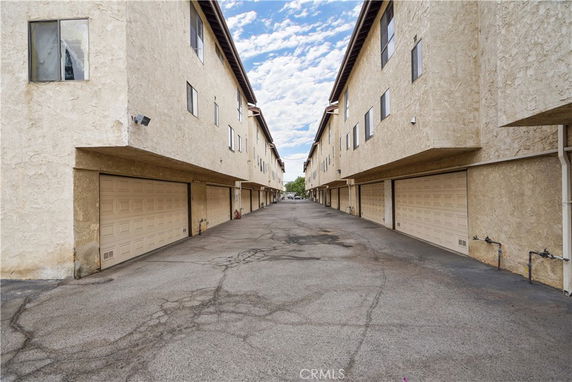 Covered parking area between two apartment buildings with garage doors.