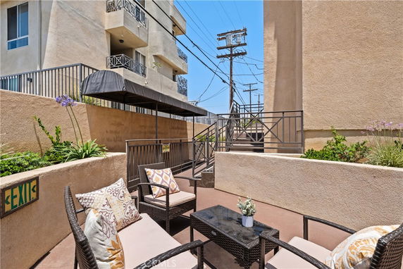 Outdoor seating area with wicker furniture and cushions near a beige building.