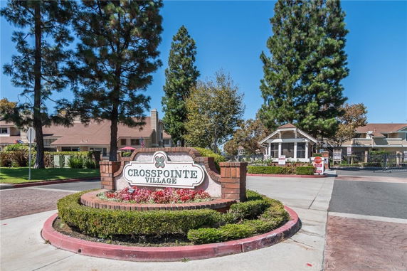 Front view of an entrance structure with a sign reading 'Crosspointe Village' near residential buildings.