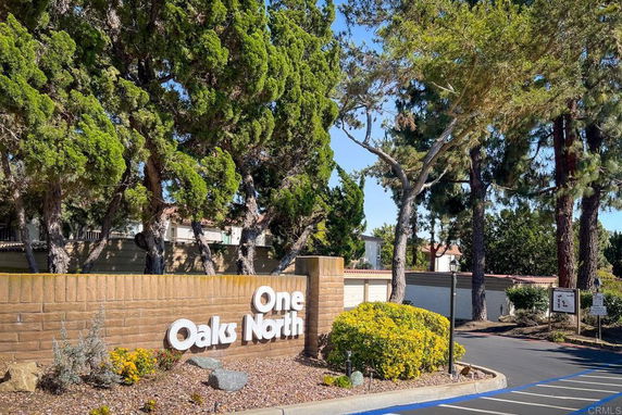 Entrance signage of a residential area named One Oaks North with surrounding trees and landscaping.