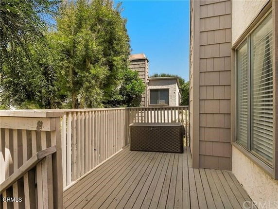 Outdoor view from a house showing a wooden deck with railing, adjacent buildings, and trees.