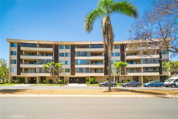 Front view of a multi-story apartment building with balconies and trees in front.
