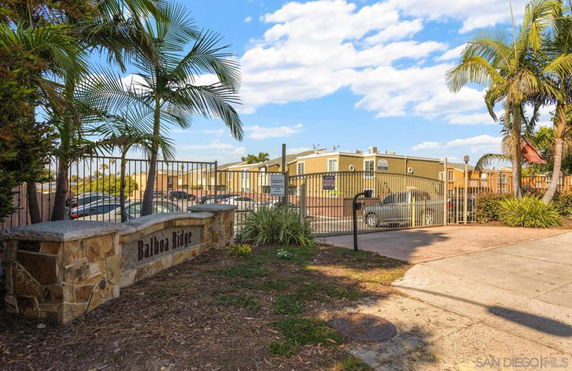 Entrance of a residential area with gated access and palm trees.