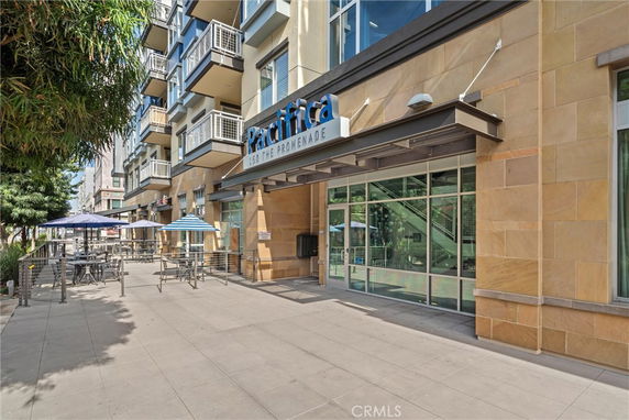 Front view of a modern multi-story building with balconies and outdoor seating area.
