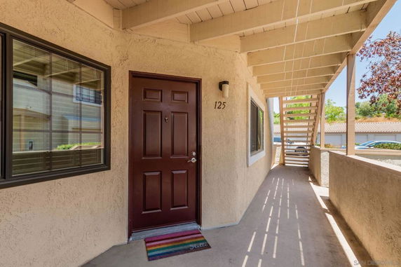 Exterior view of an entrance with a burgundy door, adjacent window, and outdoor staircase.