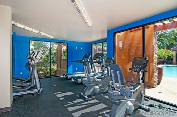 Indoor gym area with exercise bikes and treadmills near large windows.