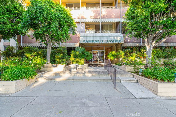 Front view of a multi-story building entrance with steps and plants.