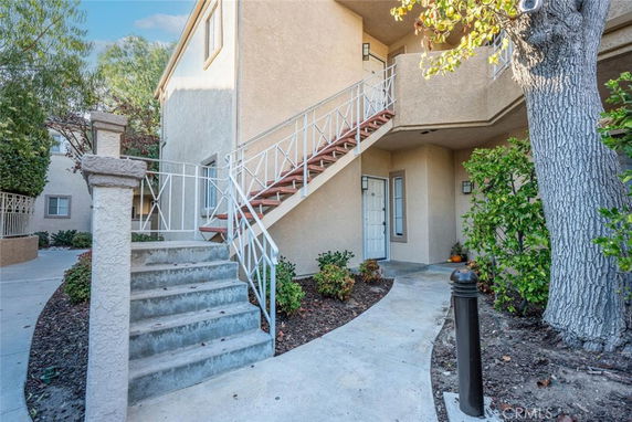Front view of a beige two-story residential building with stairs leading to the upper level.
