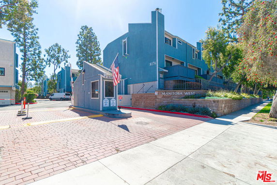 Front view of a multi-story residential building with an entrance gate and security booth.