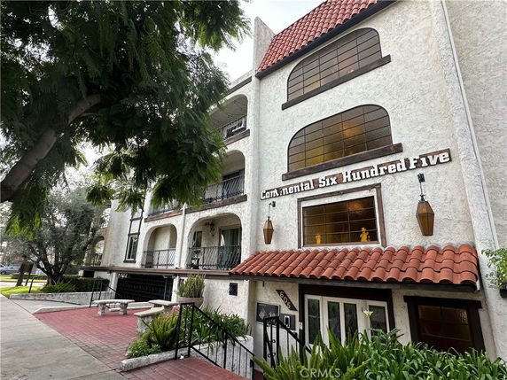 Front view of a multi-story residential building with arched windows and a red tiled roof.