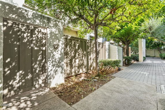 Exterior area with a wooden fence and trees casting shadows on a paved walkway.