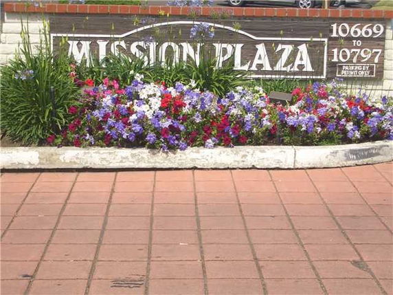 Image of a sign for Mission Plaza with colorful flowers in front.