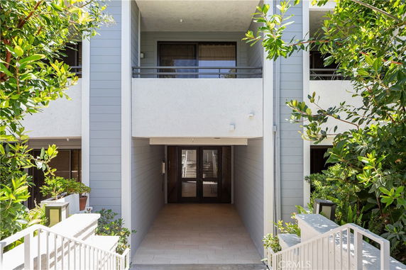 Front view of a building entrance with balconies and surrounding greenery.