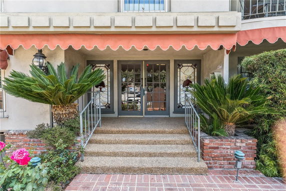 Front view of a building entrance with glass doors and decorative plants.