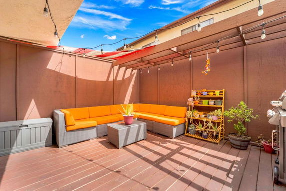 Rooftop patio with orange sofas, potted plants, and string lights under a partial shade.