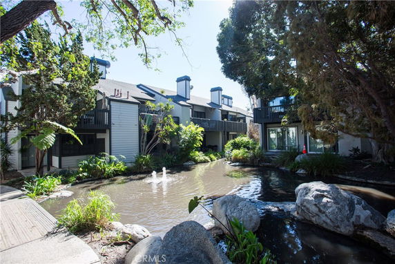 View of a residential building with balconies overlooking a pond and trees.