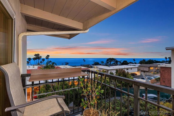 Balcony view overlooking rooftops and the ocean at sunset.