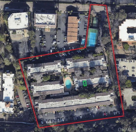 Aerial view of a complex with multiple buildings, parking areas, a swimming pool, and a tennis court.