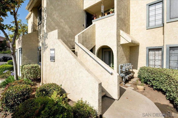 Front view of a beige apartment building with external stairs and potted plants.
