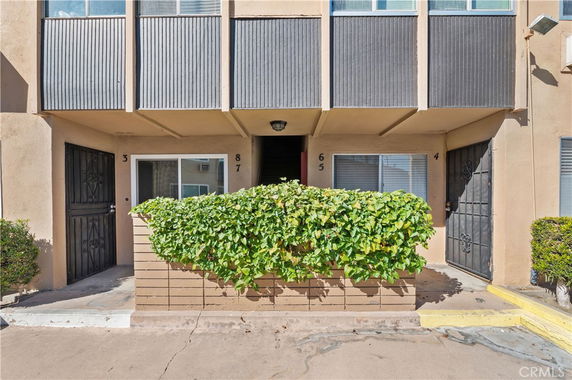 Front view of a multi-story building with small balconies and a shrub in front.