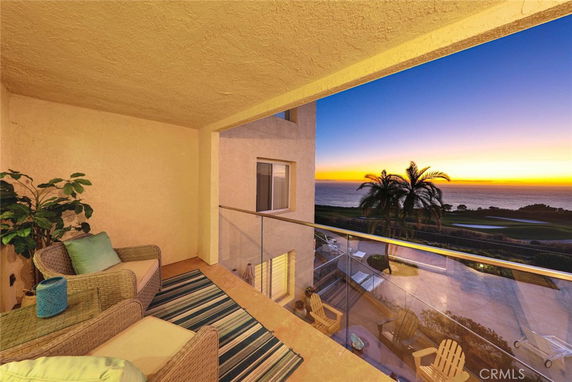Balcony view overlooking the ocean at sunset with outdoor seating.