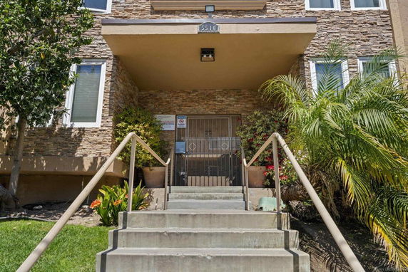 Front entrance view of a multi-story building with stone facade and plants.