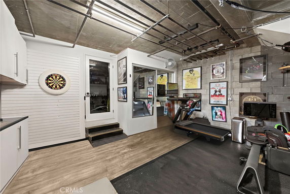 An indoor recreational space with exercise equipment, wall-mounted dartboard, and framed pictures.