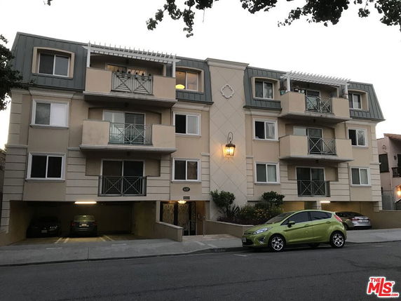 Front view of a multi-story apartment building with balconies and parking at the ground level.