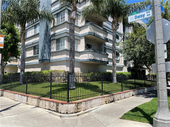 Front view of a multi-story building with balconies and surrounded by palm trees.