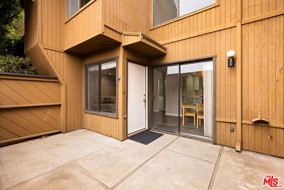 Corner view of a wooden exterior house with sliding door and windows.