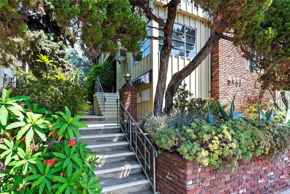 Front view of a building with brick and light exterior walls, surrounded by greenery and stairs leading up.