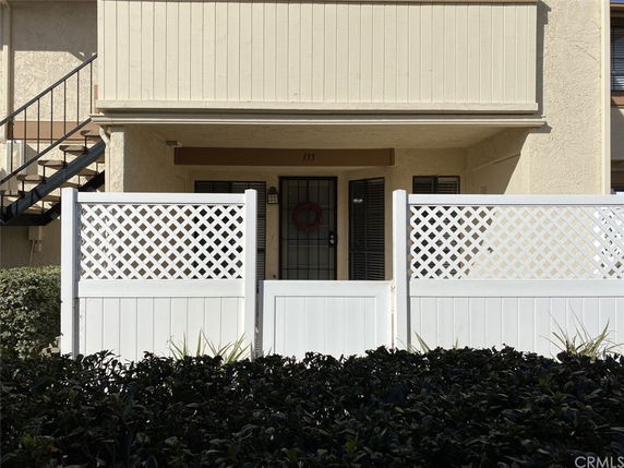 Front view of a two-story apartment entrance with a white lattice fence.