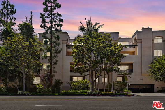Front view of a multi-story apartment building with balconies and trees.