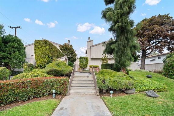 Front view of a building with stairs leading up to it, surrounded by landscaped greenery.