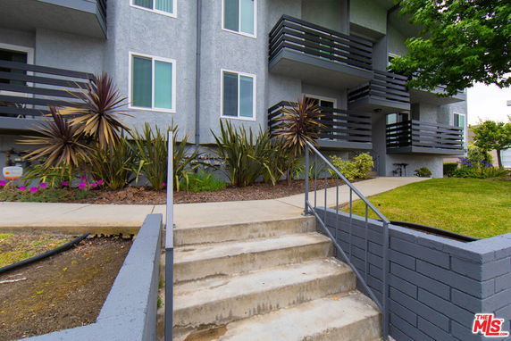 Front view of a multi-story building with balconies and a staircase leading up to the entrance.