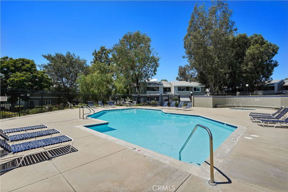 Outdoor swimming pool with surrounding lounge chairs and trees.