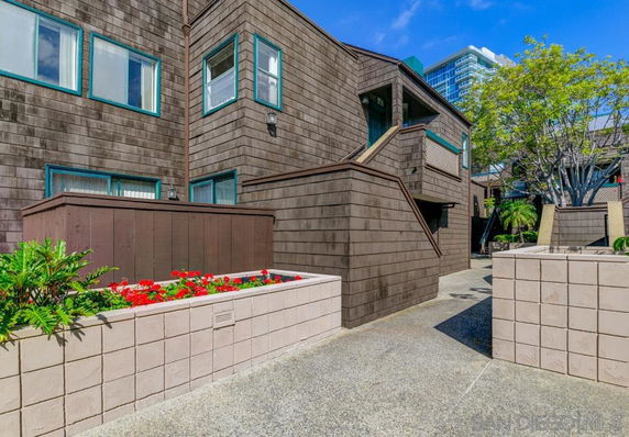 Front view of a two-story building with brown siding and teal-trimmed windows, featuring a planter with flowers.
