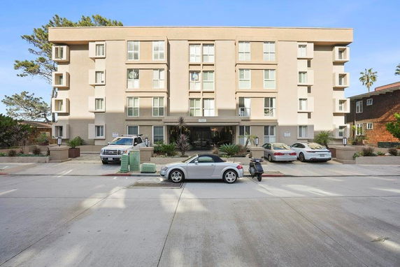 Front view of a multi-story apartment building with parked vehicles.