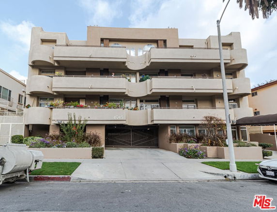 Front view of a multi-story residential building with balconies and landscaped entrance.